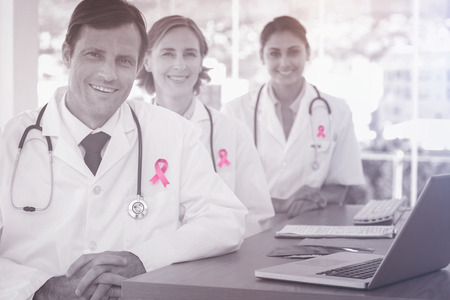 Breast cancer awareness ribbon against portrait of smiling doctors at deskの写真素材