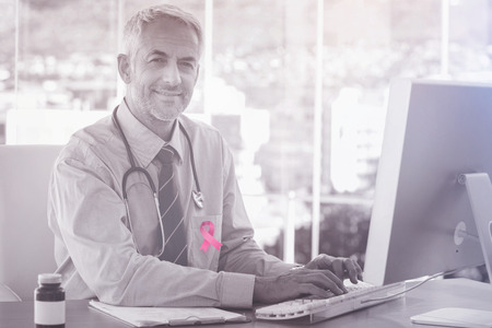 Breast cancer awareness ribbon against portrait of smiling doctor working on computerの写真素材