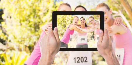 Cropped hand holding digital tablet against portrait of young athlete women forming huddles