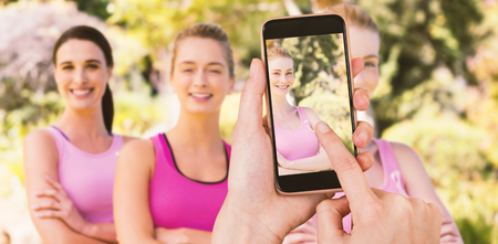 Hands touching smart phone against portrait of confident volunteers supporting breast cancer awarenessの写真素材