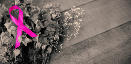 High angle view of pink Breast Cancer Awareness ribbon on flowers over wooden tableの写真素材