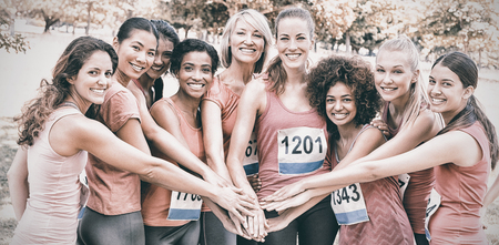 Portrait of female breast cancer marathon runners stacking hands in parkの写真素材