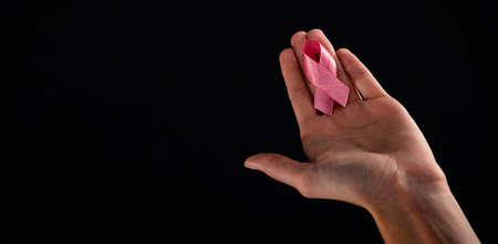 Cropped image of hand holding pink ribbon against black backgroundの写真素材