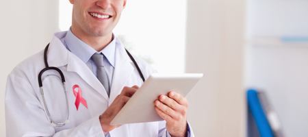 Breast cancer ribbon against portrait of smiling doctor with his tabletの写真素材