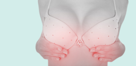 Mid section of woman in bra touching breast for cancer awareness against blue backgroundの写真素材