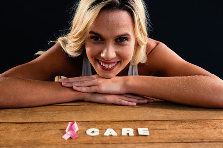Portrait of smiling young woman by table with pink ribbon and care textの写真素材