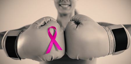 Mid section of smiling woman with boxing gloves and pink ribbon while standing against gray backgroundの写真素材