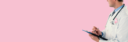 Doctor writing with pen on clipboard against pink backgroundの写真素材