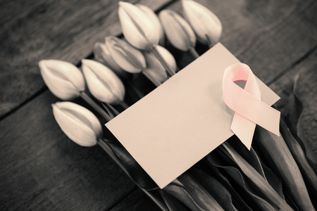 High angle view of pink Breast Cancer Awareness ribbon with blank card on tulips over wooden tableの写真素材