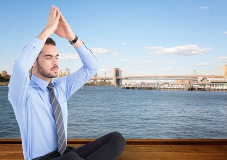 Digital composite of Business man meditating against water and skylineの写真素材