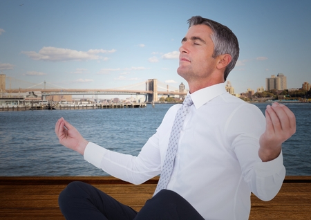 Digital composite of Business man meditating against water and skylineの写真素材
