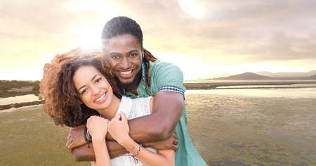 Digital composite of Couple embracing against river and evening sky with flare