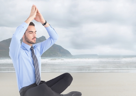 Digital composite of Business man meditating against blurry beachの写真素材