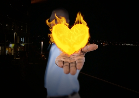 Digital composite of Man with hand spread of with heart fire icon over.  City at nightの写真素材