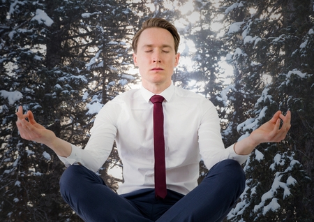 Digital composite of Business man meditating against snowy trees with sun shining throughの写真素材