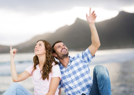 Digital composite of Couple sitting and pointing against blurry beach