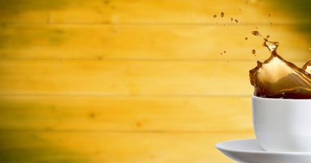 Digital composite of White cup with coffee splashing against blurry yellow wood panelの写真素材