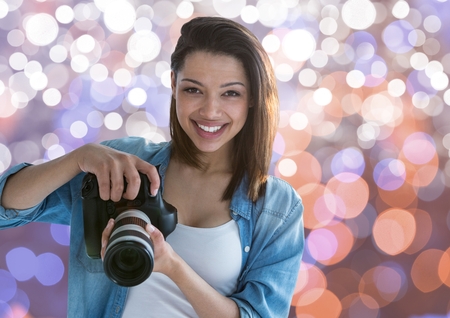Digital composite of young photographer smiling with the camera on hands. Brown white and blue bokeh backgroundの写真素材