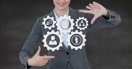 Digital composite of Business woman interacting with people in cogs graphics against grey backgroundの写真素材