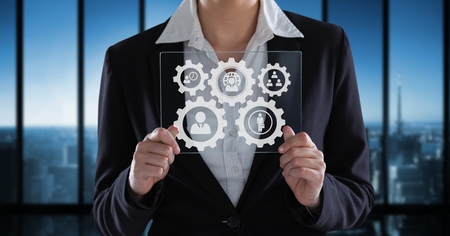 Digital composite of Business woman interacting with people in cogs graphics against office backgroundの写真素材