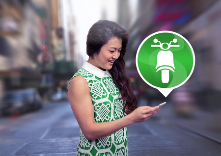 Digital composite of Woman holding phone with motorbike icon in cityの写真素材
