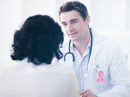 Breast cancer awareness ribbon against handsome doctor talking with his patient for the annual checkupの写真素材