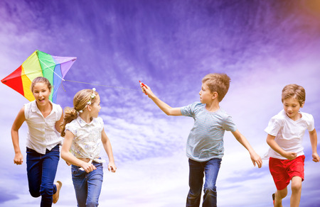Full length of boy holding kite running with friends against view of cloudy skyの写真素材