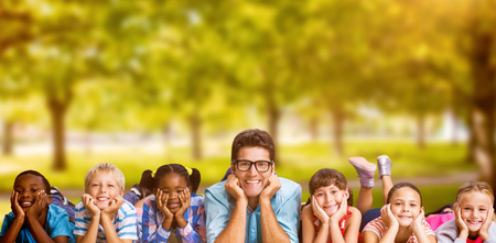 Portrait of teacher lying down with students against trees in grassy landscape