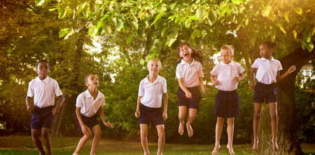 Happy students in school uniforms against trees and meadow in the parkの写真素材