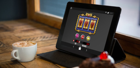Slot machine on mobile screen against digital tablet with pastry and coffee cup on tableの写真素材