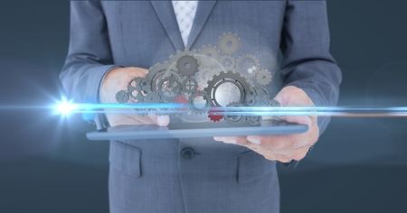 Digital composite of business man holding tablet with 3 d cogs on itの写真素材