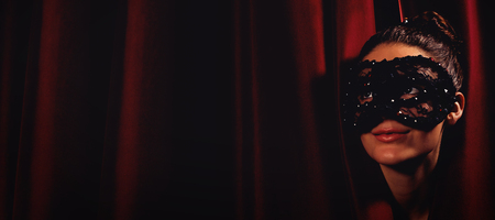 Female artist in mask peeking through curtain at stageの写真素材