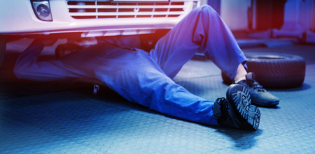 Mechanic lying and working under car at the repair garageの写真素材