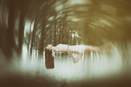 Girl in white dress floating in air against forest full of smokeの写真素材