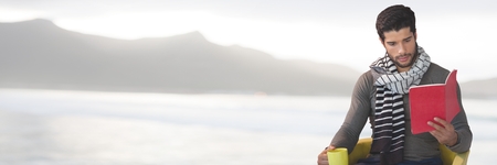 Digital composite of Man reading with cup by sea mountainsの写真素材