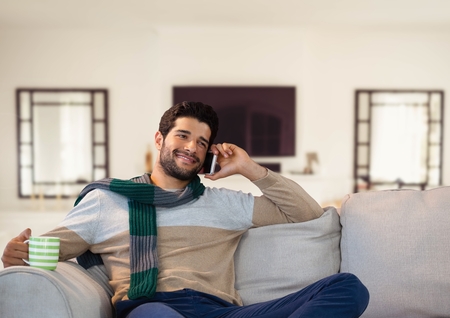 Digital composite of Man in Autumn with phone and cup on couch at homeの写真素材