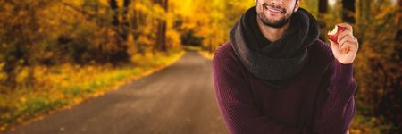 Portrait of young man holding apple against country road along trees in the lush forest