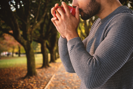 Side view of thoughtful man having coffee against footpath amidst trees at parkの写真素材