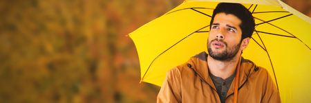 Thoughtful man with yellow umbrella against tree growing outdoorsの写真素材