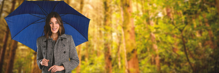 Portrait of young woman holding umbrella against low angle view of treesの写真素材