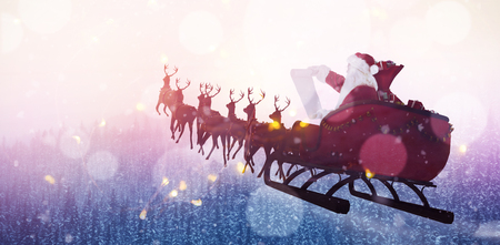 Santa Claus riding on sled during Christmas against snow covered trees during winterの写真素材