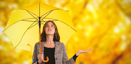 Full length of woman holding umbrella while gesturing against branches and autumnal leavesの写真素材