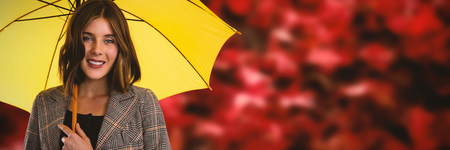 Portrait of smiling woman with yellow umbrella against red maple leaves by trees trunk during autumnの写真素材