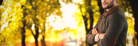 Young man with arms crossed against white background against defocused image of trees growing at parkの写真素材