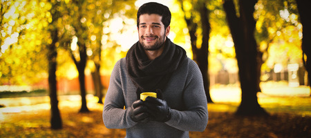 Smiling man looking away while holding mug of coffee against defocused image of trees growing at parkの写真素材