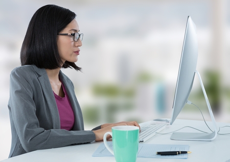 Digital composite of Businesswoman at desk with computer with bright backgroundの写真素材