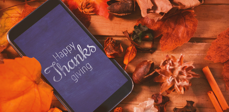 Thanksgiving greeting text against mobile phone on wood table surround of leaf