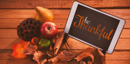 Thanksgiving greeting text against touch pad on leaf on wood tableの写真素材