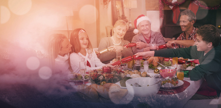 Clouds covering snowcapped mountains against sky against smiling family pulling christmas crackers at the dinner tableの写真素材