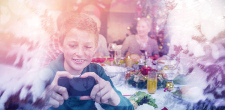 Scenic view of snow covered trees against young boy holding smartphone during christmas dinnerの写真素材